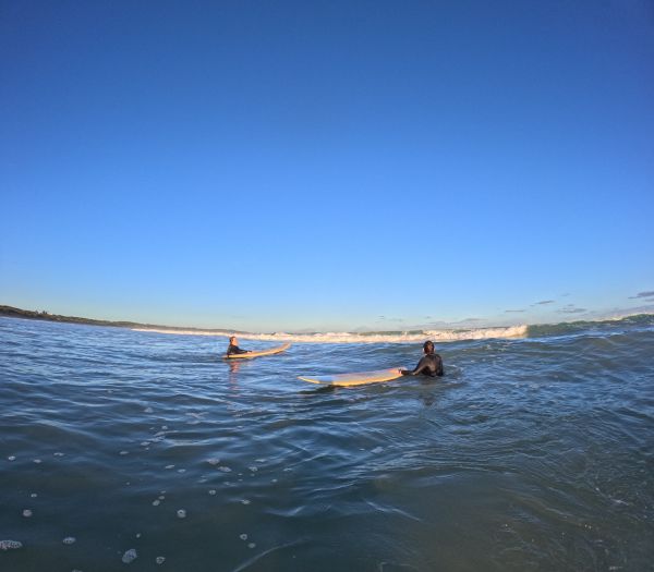 Two women standing in the ocean with surfboards. The sun is shining