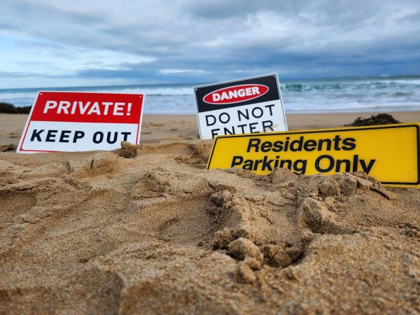 Three signs are wedged into the wet sand in front of the ocean. The signs say 