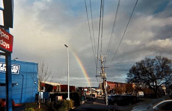 A rainbow in the distance in a urban setting with powerlines and buildings