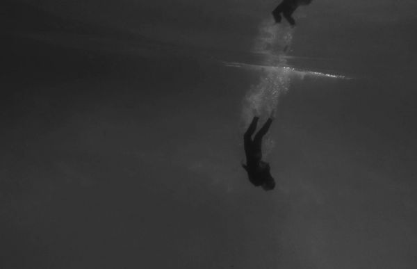 An underwater photo of a woman diving down to the ocean floor head first. Her body is a meter below the surface and oxygen bubbles are floating up behind her.