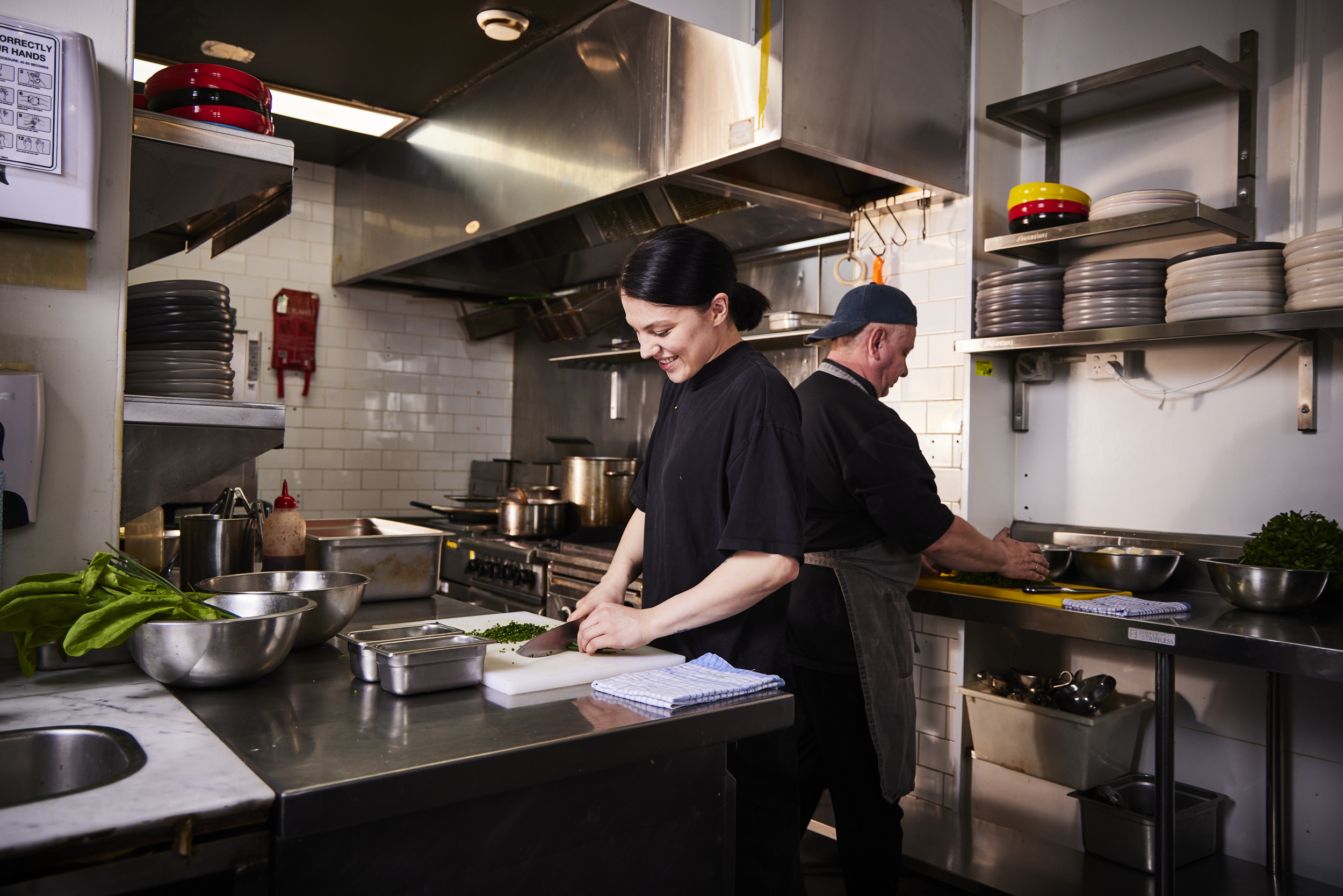 Two people in chef's uniforms preparing food in a professional kitchen