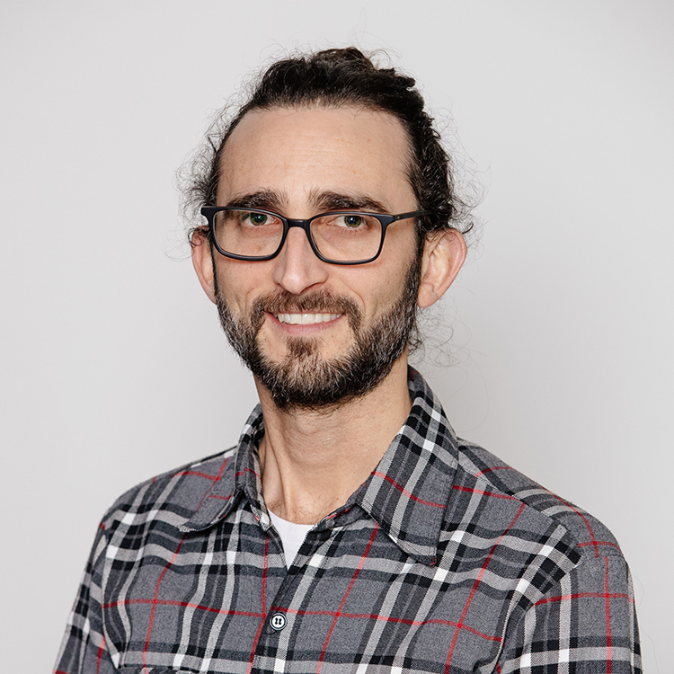 Juan Tellez wearing a grey and red plaid shirt and square framed glasses