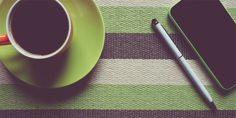 A cup of black coffee, a pen and an iPhone all sitting on a green placemat