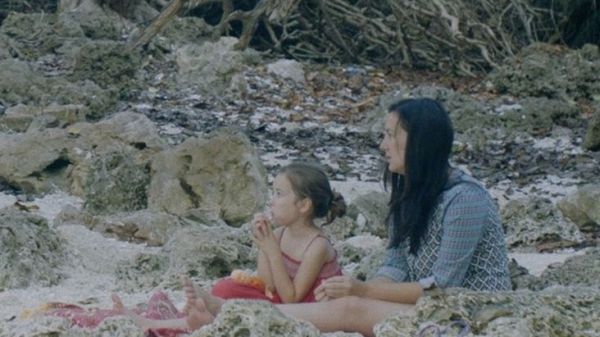 Photo of a woman and a young girl sitting on a rocky beach