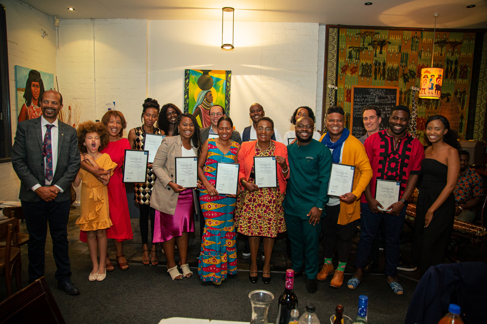 Group photo of 20 people at an African restaurant. They are smiling at the camera and many are holding certificates.